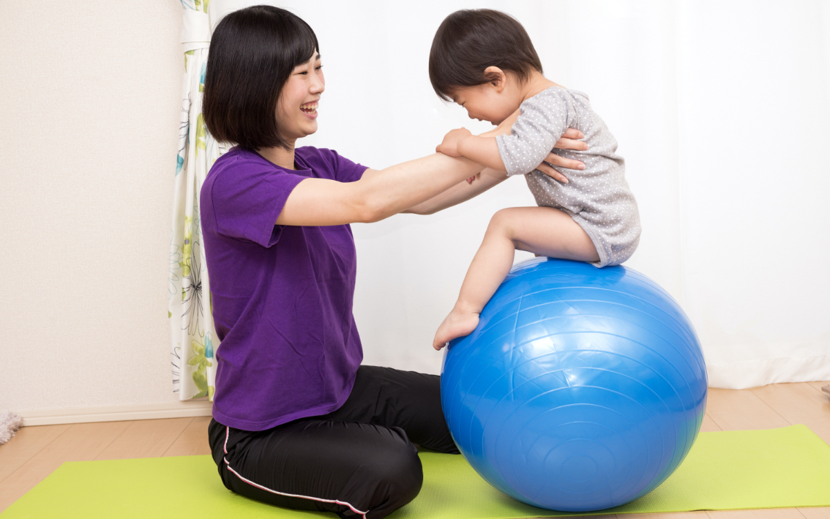 バランスボールに乗る子供と支える大人